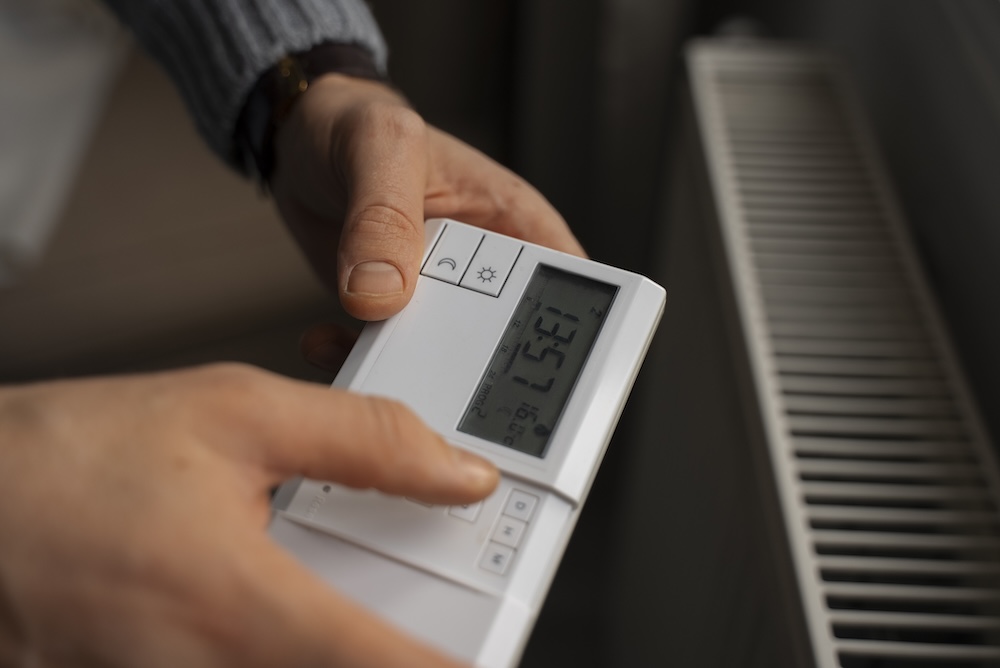 l'image montre un installateur de chauffage électrique en train de programmer un thermostat dans une maison de 100m2